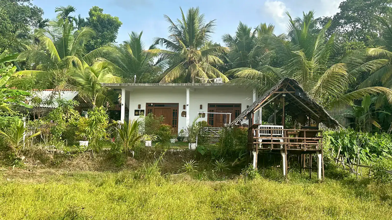 Die Villa Mihira zwischen Kokospalmen, davor der Garten und die Hütte auf Stelzen